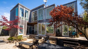 A modern two-story house with large windows, a deck, and outdoor seating.