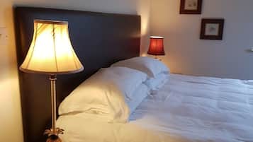 Una cama bien hecha con sábanas blancas, un cabecero oscuro y dos lámparas de noche.