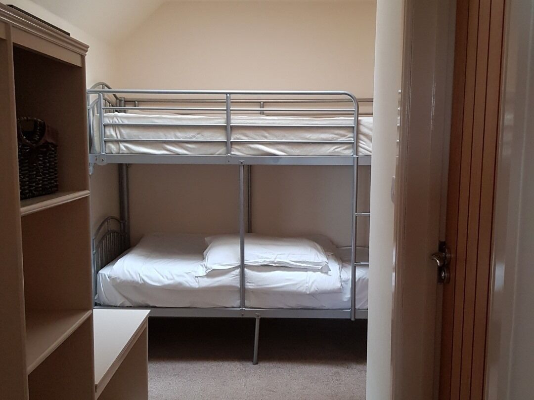 Un letto a castello con struttura in metallo, biancheria da letto bianca e una porta in legno.