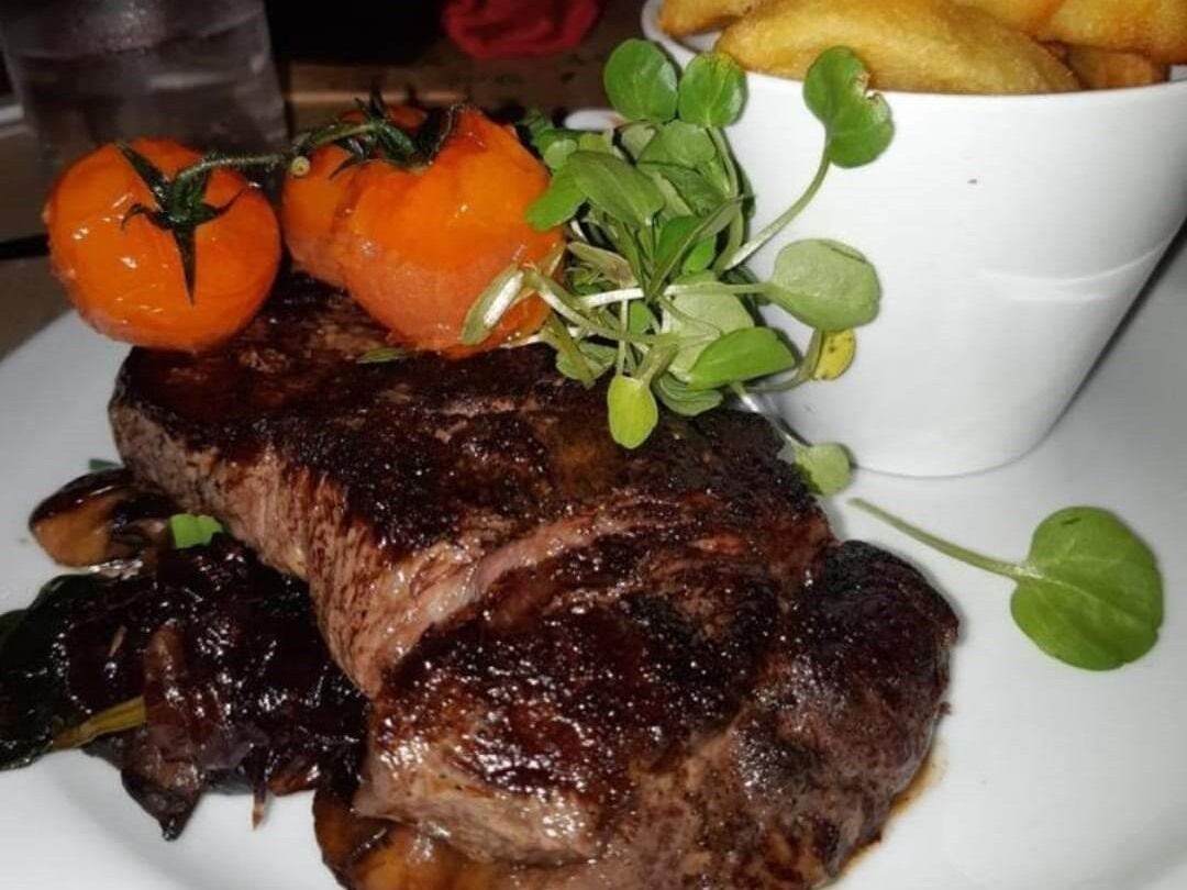 A steak with cherry tomatoes and greens on a plate.