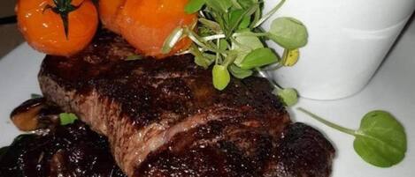 A steak with cherry tomatoes and greens on a plate.