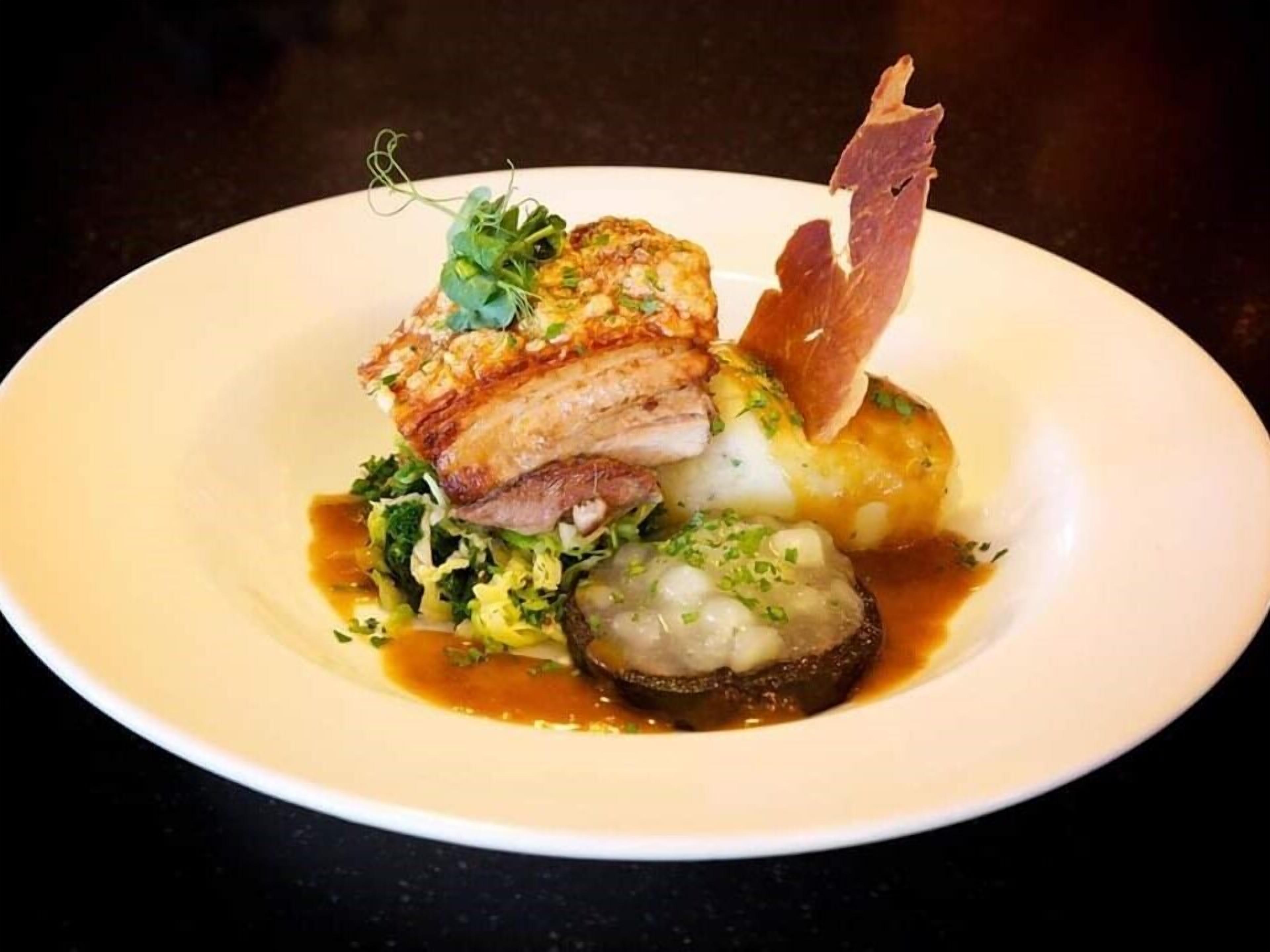 Une assiette blanche contenant un plat composé d’un morceau de viande, d’un légume rond et d’une garniture.