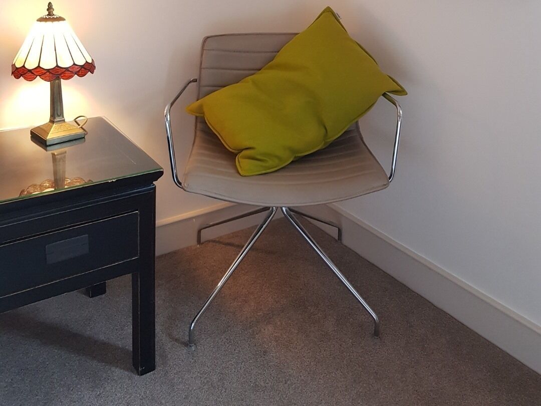 A chair with a metallic frame and a cushion, a small table with a lamp, and a carpeted floor.