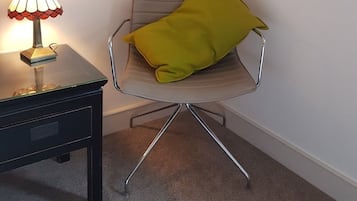A chair with a metallic frame and a cushion, a small table with a lamp, and a carpeted floor.