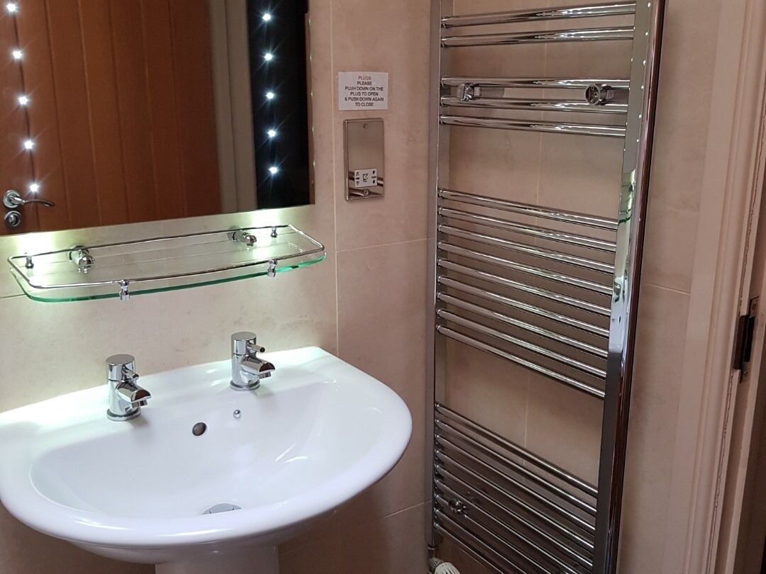 A bathroom with a white sink, two faucets, a glass shelf above the sink, and a towel rack with multiple horizontal bars.