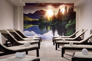 Un cuarto de spa con sillones reclinables y un gran mural de un lago de montaña al atardecer.