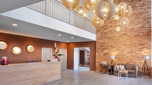 Un lobby moderno de hotel con un mostrador de recepción de madera, una zona de estar con sofá y mesa de centro, y un gran panel de madera.