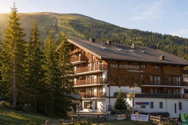 A multi-story building with balconies, labeled 'Das Alpenhaus,' located in a mountainous area with visible greenery and a clear sky. - Das Alpenhaus Katschberg.1640 (Sankt Michael im Lungau)