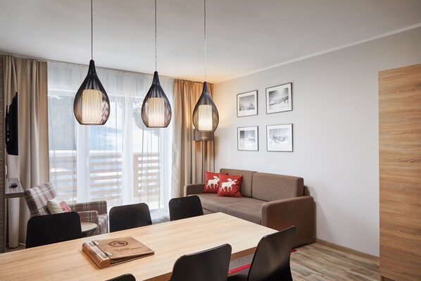 Una habitació d'hotel moderna amb zona de menjador, un sofà amb un coixí de tròs vermell i quadres a la paret.