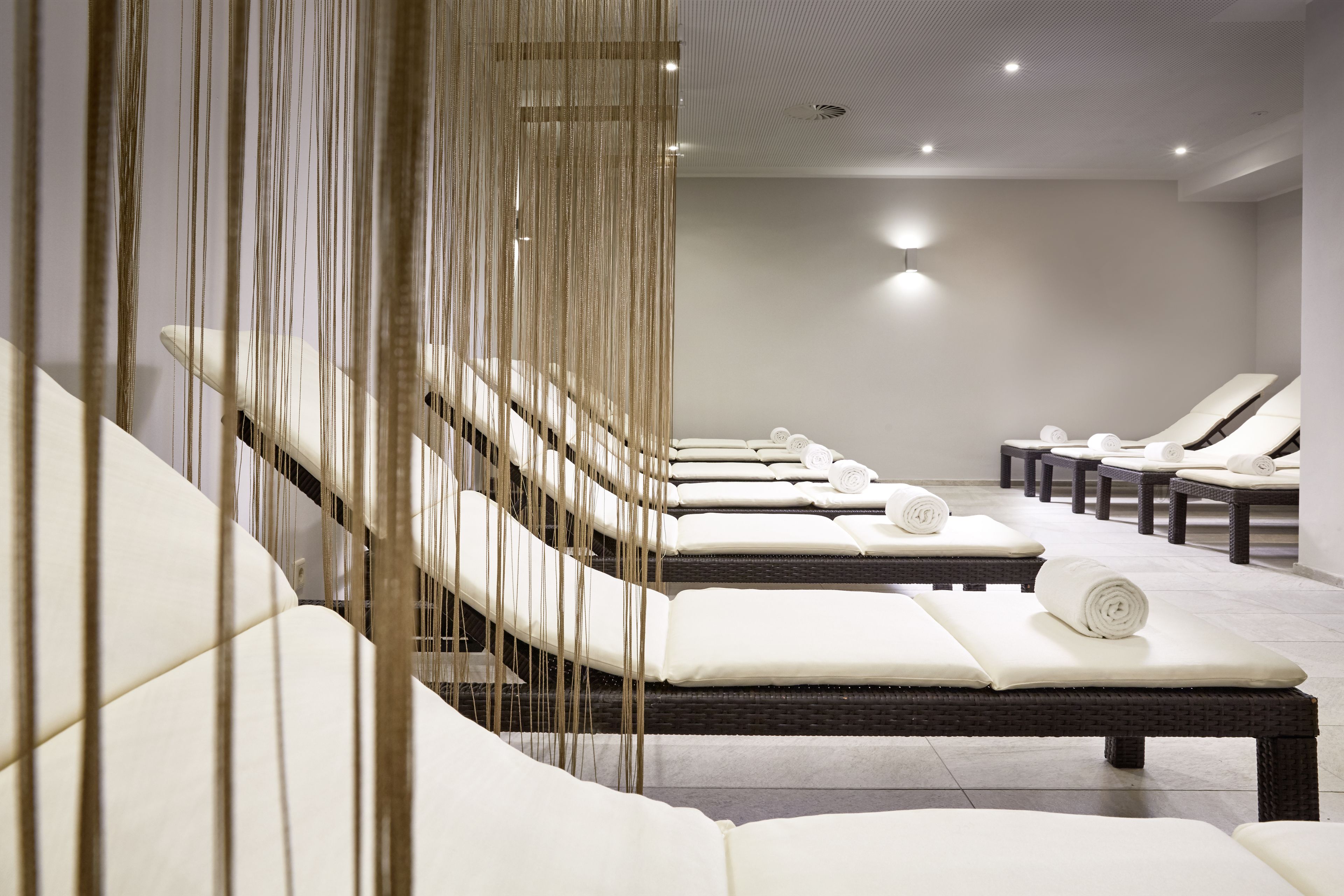 Un cuarto de spa con varias mesas de masaje, cada una con una toalla enrollada.