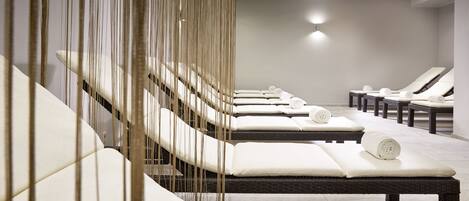 Un cuarto de spa con varias mesas de masaje, cada una con una toalla enrollada.