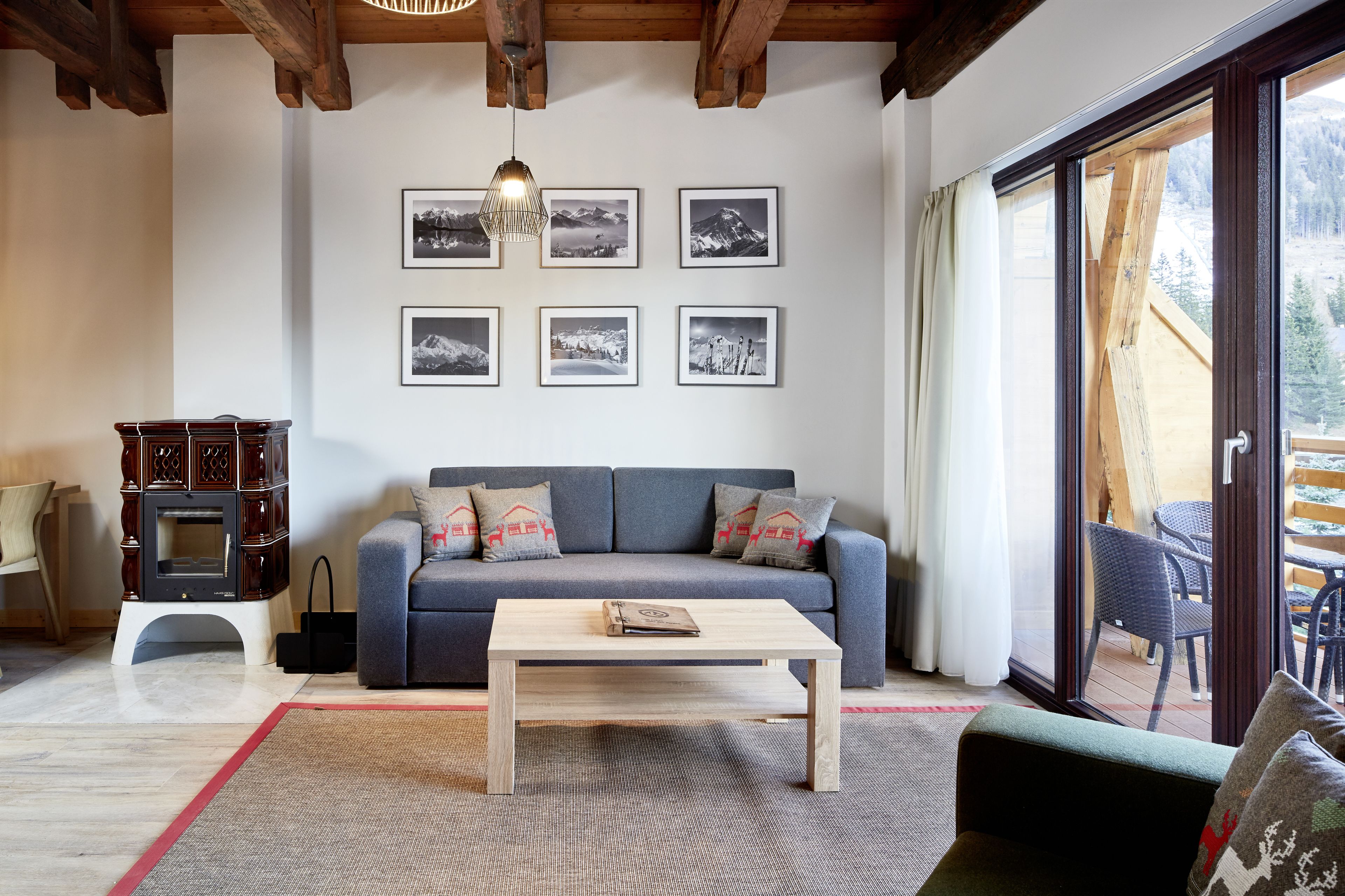 A living room with a sofa, coffee table, and fireplace. There are six framed pictures on the wall and a view of the outdoors through a glass door.