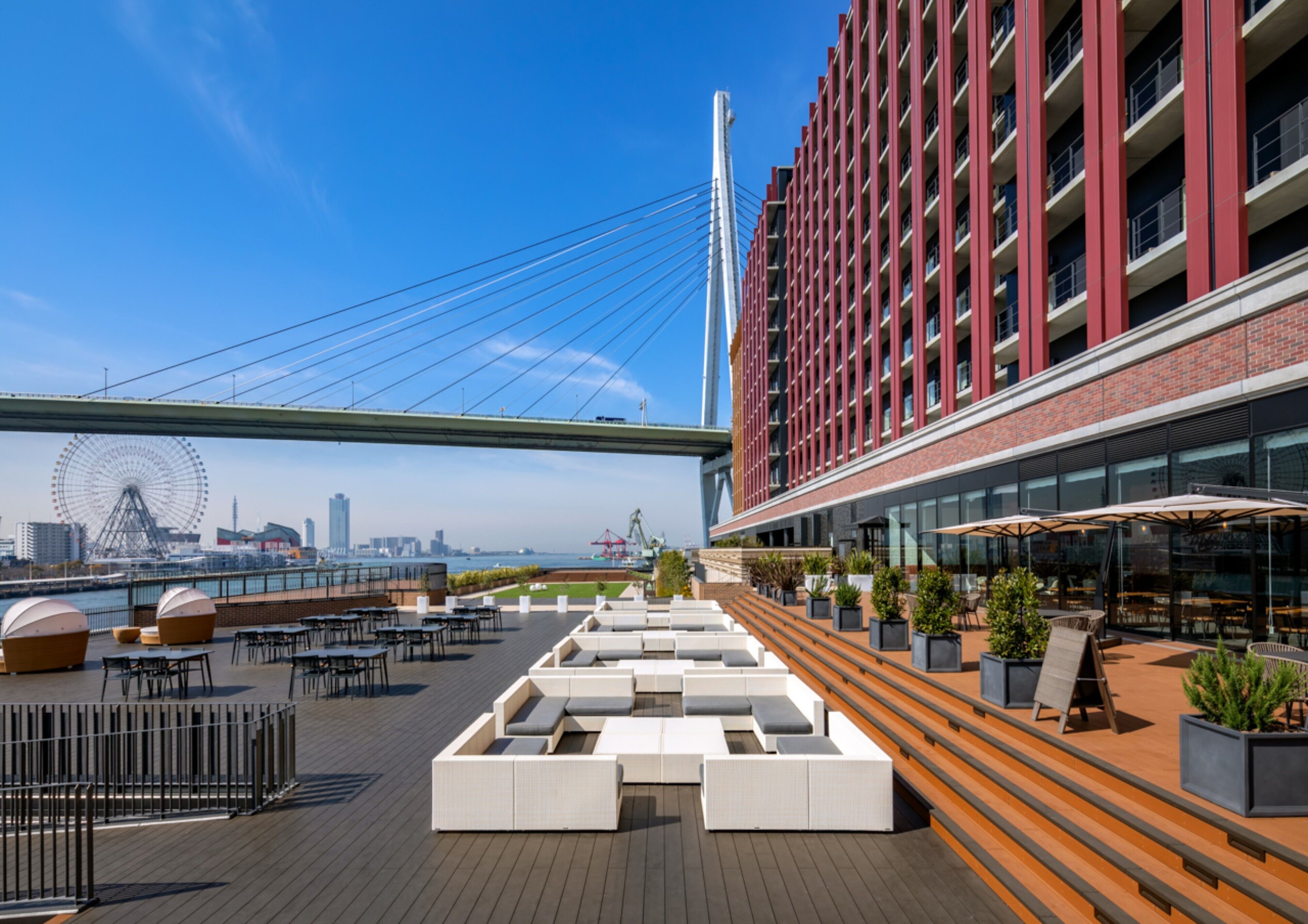 A rooftop terrace with outdoor seating, a view of a city skyline, and a modern building with red accents.