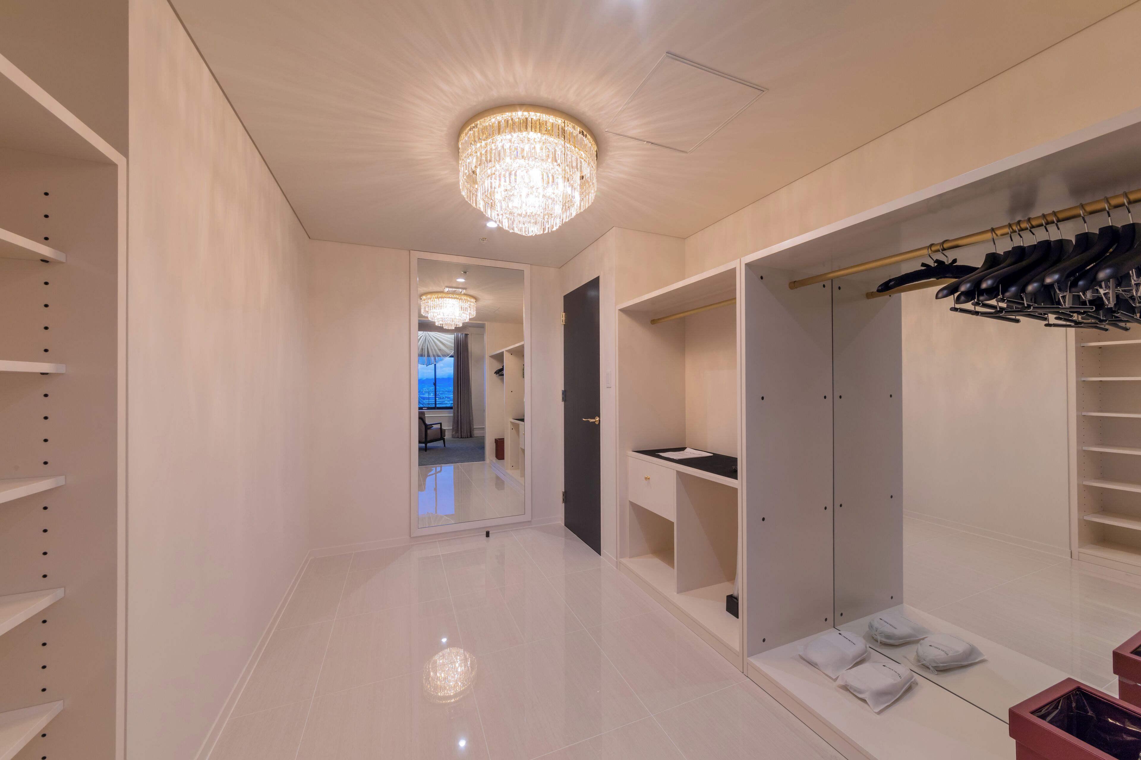 A modern walk-in closet with a chandelier, shoe rack, and mirrored closet doors.