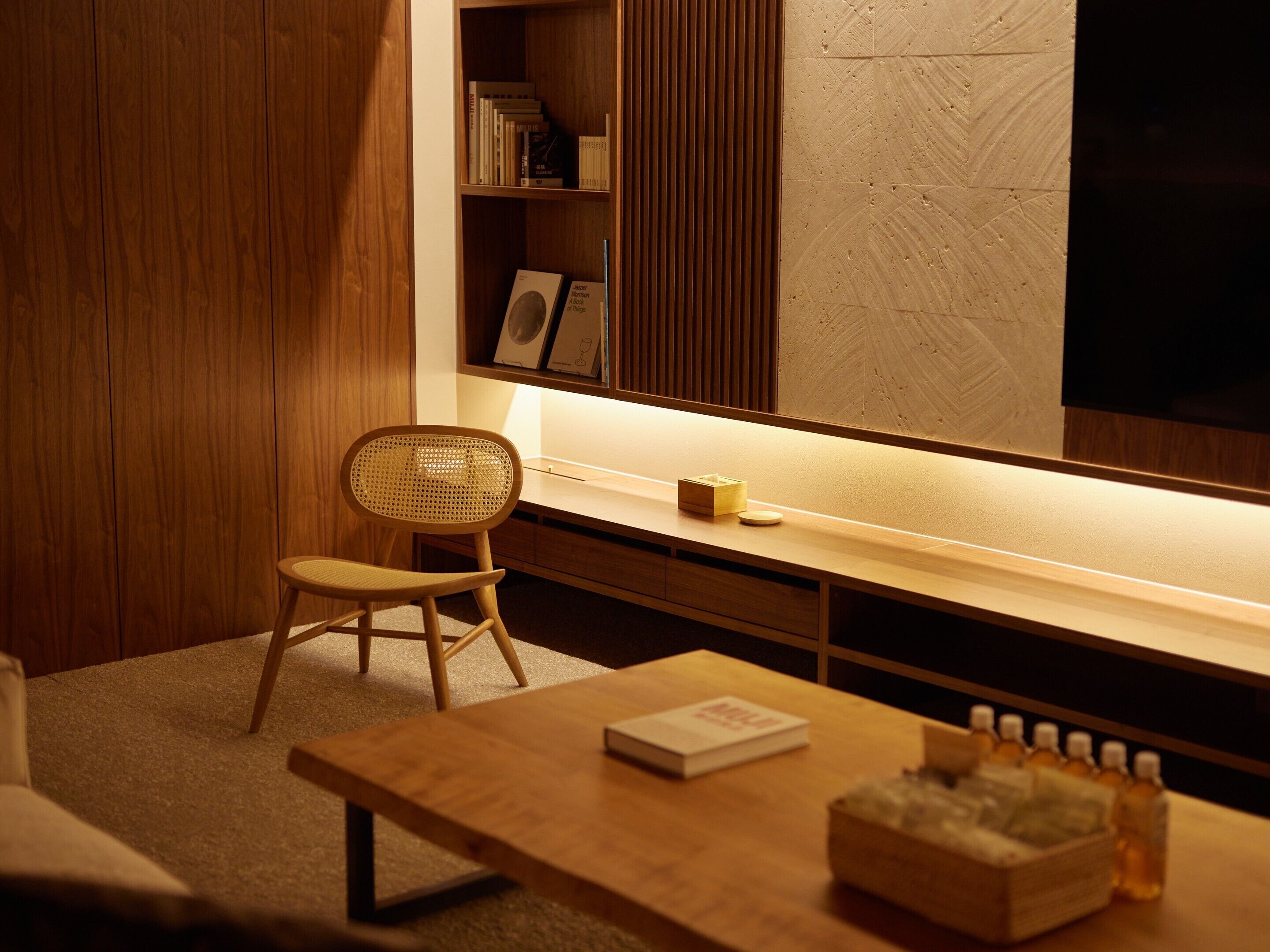 A modern room with a wooden desk, a wicker chair, a bookshelf, and a large mirror.