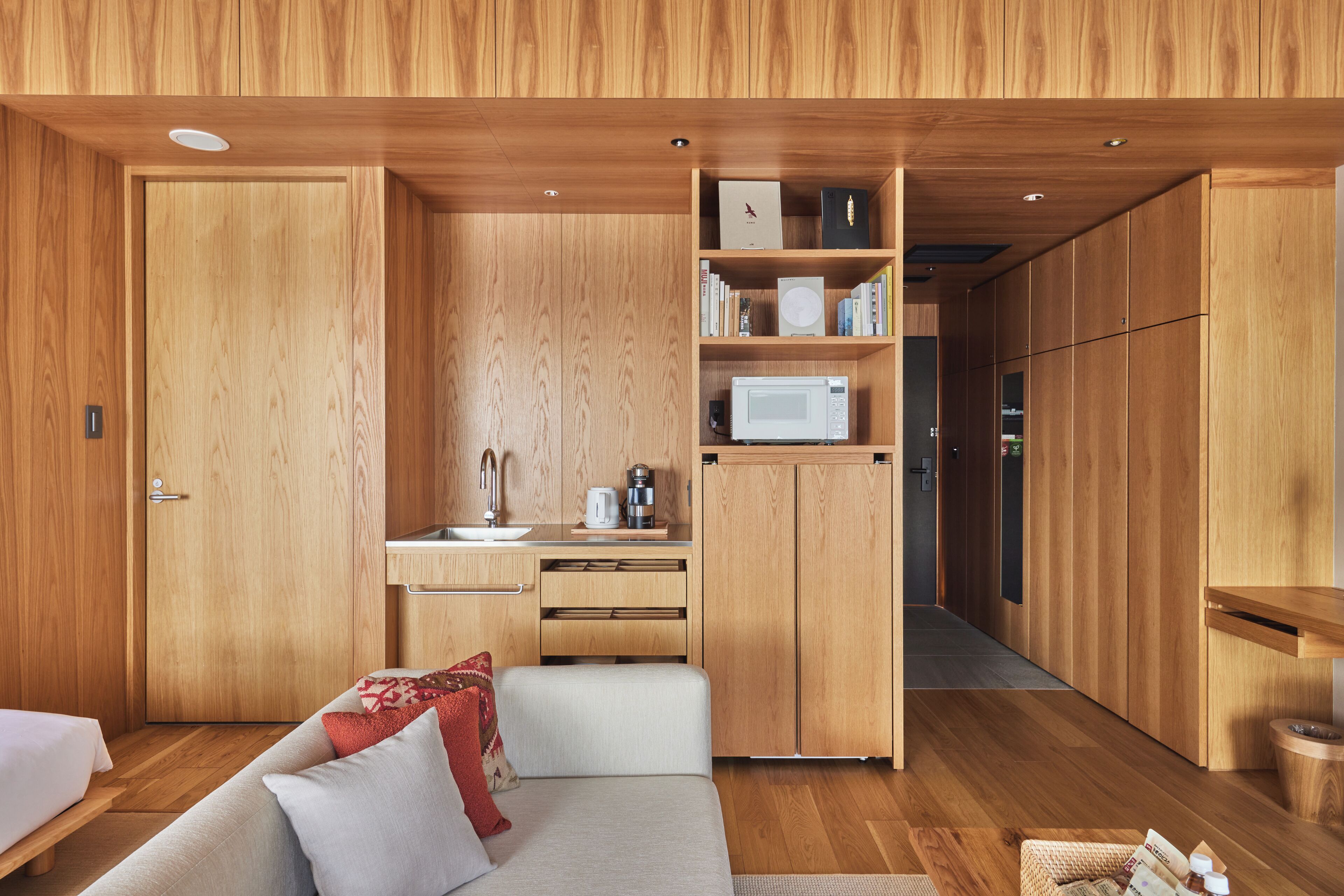 Une pièce compacte et moderne, avec un intérieur en bois, une kitchenette, un canapé avec des coussins et un petit coin repas.