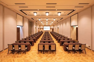 A conference room with rows of tables and chairs, a projector screen, and a wooden floor.