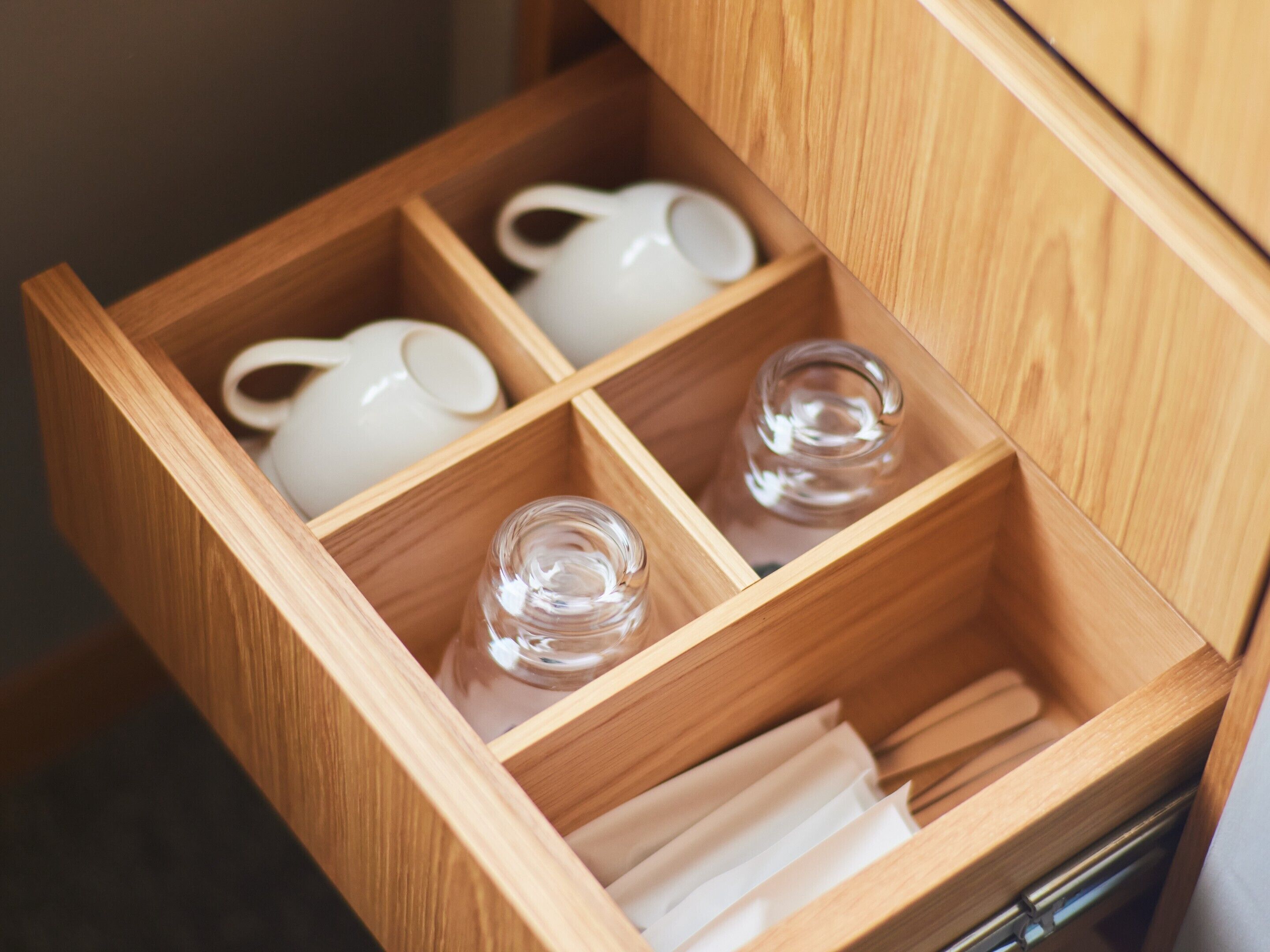 Un tiroir en bois, doté de compartiments, contenant une théière blanche, un bocal en verre et une bouteille en verre.