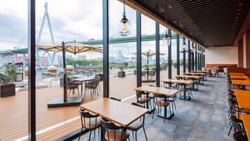 En restaurang med uteservering, stora fönster och utsikt över en bro.