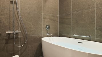 A modern bathroom with a freestanding bathtub, a handheld showerhead, and a toilet paper holder.