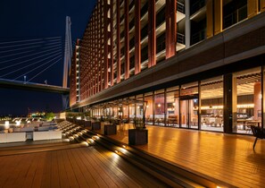 A modern hotel with a covered outdoor area, a view of a bridge, and a restaurant with outdoor seating. - LIBER HOTEL OSAKA (Osaka)