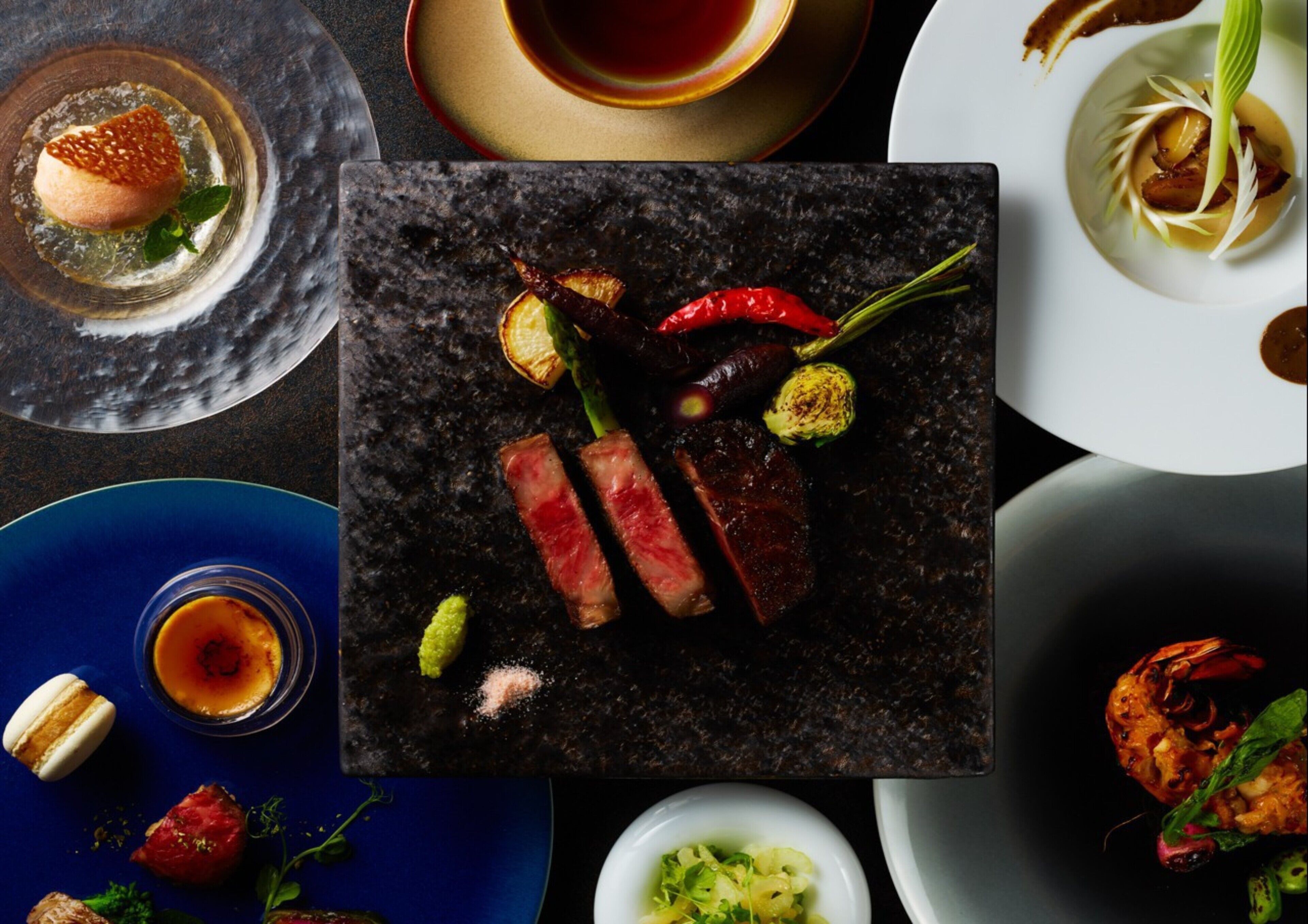 A variety of dishes including a steak, vegetables, and a dessert.