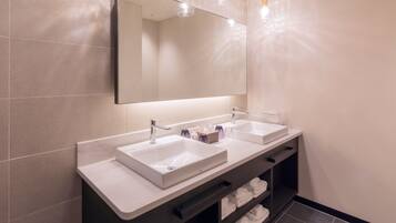 A modern bathroom with two sinks, a large mirror, and a towel rack.