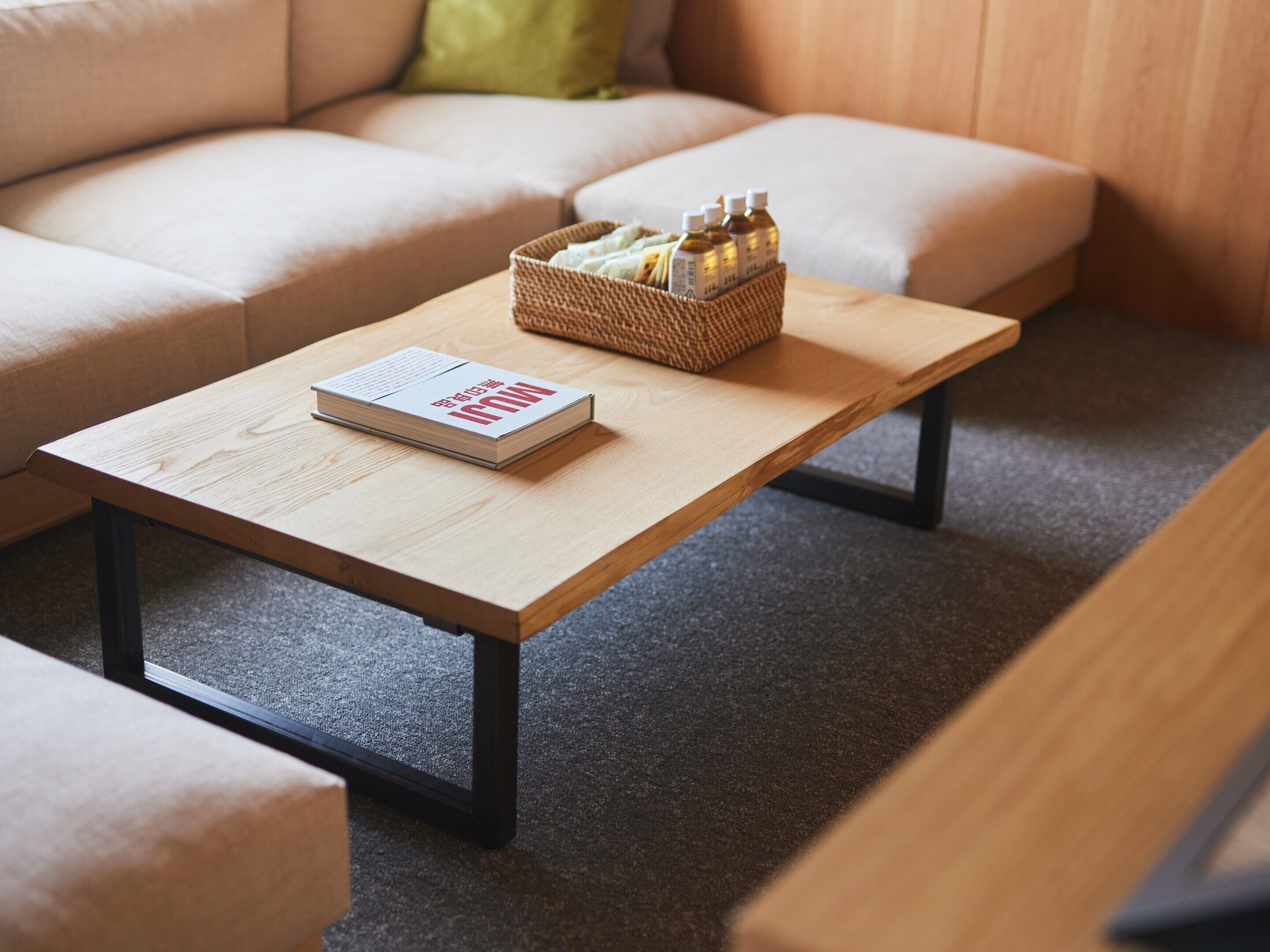 Un salon moderne avec une table basse en bois, un livre et un panier rempli de bouteilles.