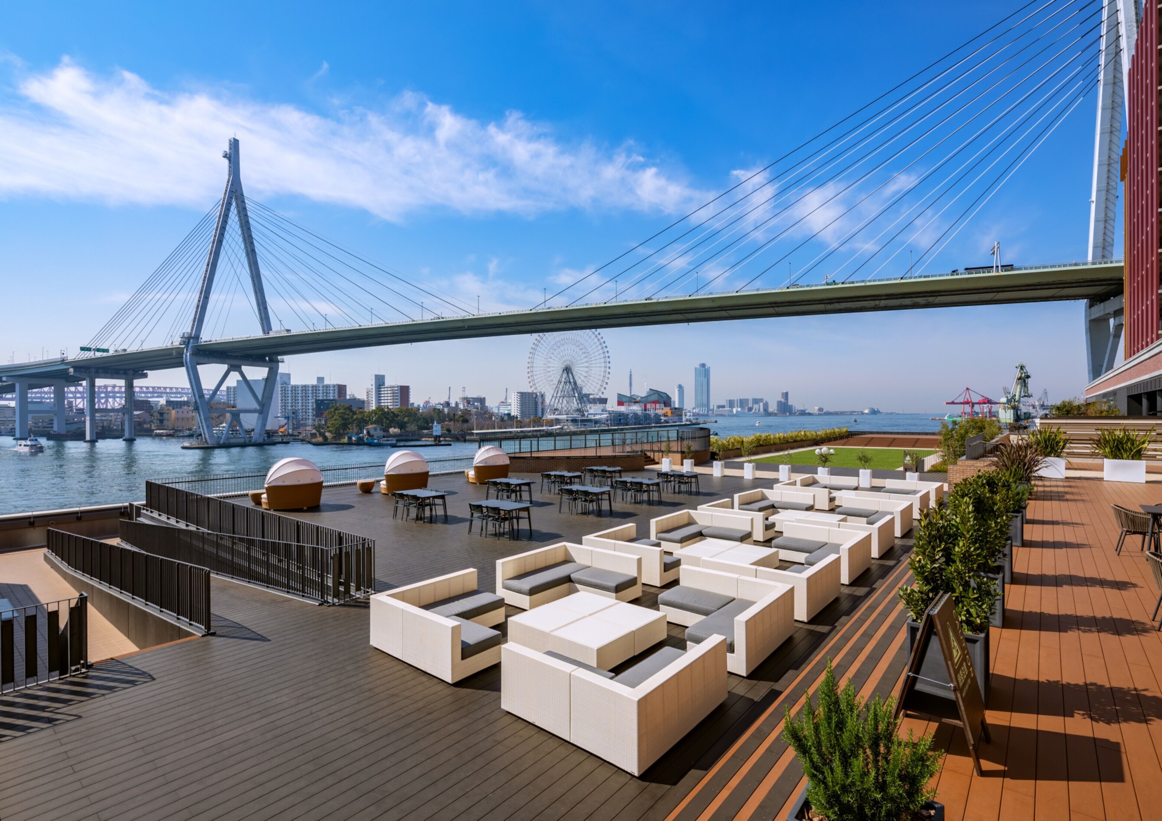 Une terrasse sur le toit avec des sièges en plein air, une vue sur les gratte-ciel de la ville et un grand pont suspendu en arrière-plan.