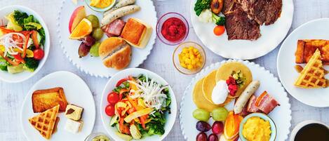 A table with various breakfast dishes including waffles, eggs, sausages, and salads.