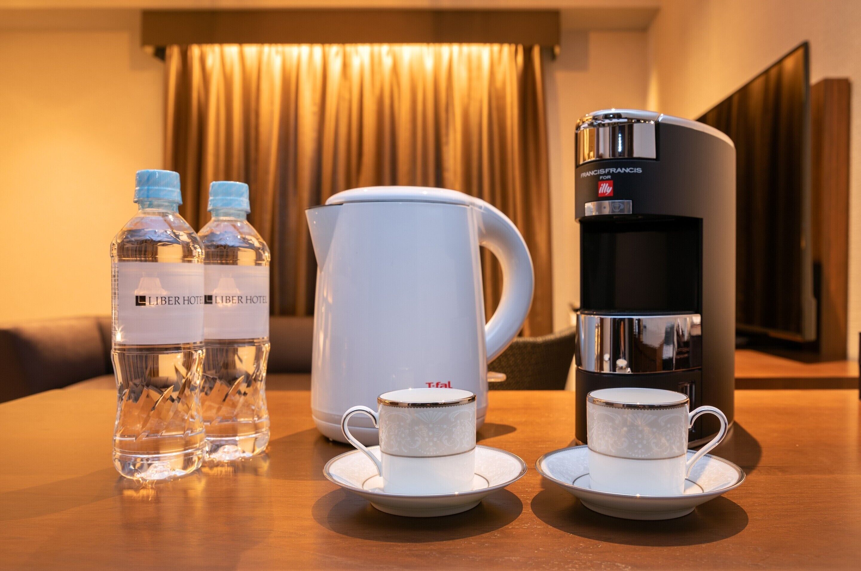 A hotel room with a table set for tea, including two water bottles, a teapot, and a coffee maker.