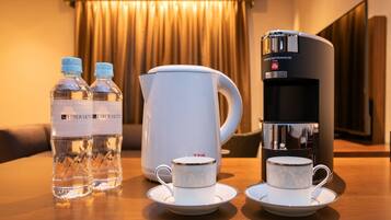 Habitación de hotel con una mesa preparada para té, incluyendo dos botellas de agua, una tetera y una cafetera.