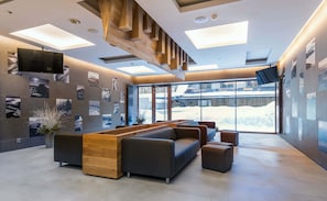 A modern lobby with a wooden reception desk, leather seating, and a large window offering a snowy view. - Hotel Pecr Deep (Pec pod Snezkou)