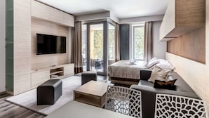 A modern hotel room with a large flat-screen TV, a bed with a view to the outdoors, a seating area with a coffee table, and a built-in entertainment unit. - Hotel Pecr Deep (Pec pod Snezkou)