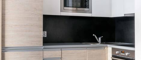 A modern kitchen with wooden cabinets, a stainless steel microwave, a black countertop, and a white chair.