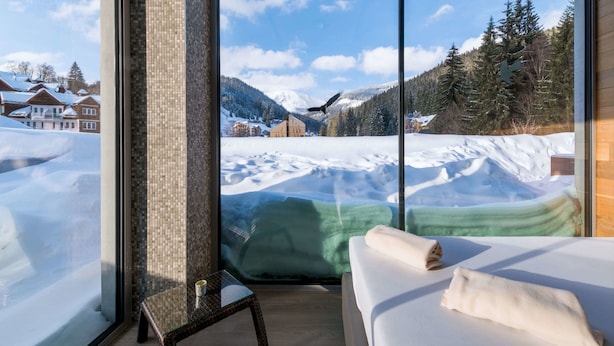 A hotel room with a large window offering a snowy mountain view, a bed with a white cover, and a glass table with a cup. - Hotel Pecr Deep (Pec pod Snezkou)
