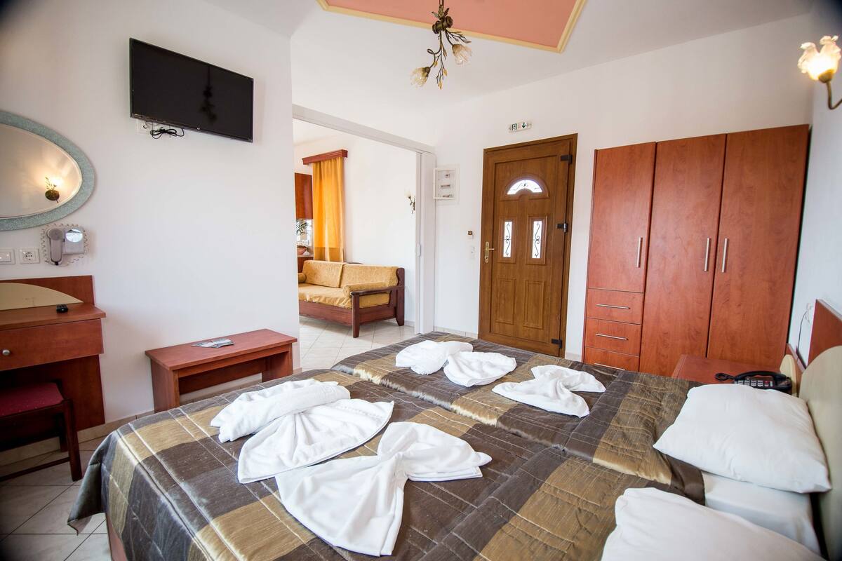 A hotel room with a bed, wooden wardrobe, desk, and a television.