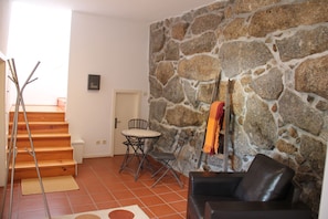 Una sala de estar con una pared de piedra, una escalera de madera, un sofá de cuero negro y una pequeña mesa redonda con sillas.