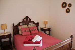 Un lit bien fait, avec une literie rouge, deux lampes de chevet et des coussins à motifs floraux.