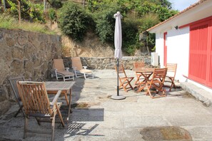 Une terrasse extérieure avec un sol en pierre, des meubles en bois et un bâtiment rouge en arrière-plan.