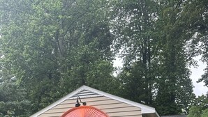 A single-story house with a pitched roof, a small porch, and a window with a white frame and a red arch. - Super Clean Home on a Quiet Cul-De-Sac in the Woods. (Lewes)