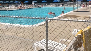 A swimming pool with lounge chairs and umbrellas, surrounded by a fence. - Super Clean Home on a Quiet Cul-De-Sac in the Woods. (Lewes)