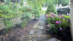 A wooden deck leading to a house with a garden path, surrounded by trees and shrubs. - Super Clean Home on a Quiet Cul-De-Sac in the Woods. (Lewes)