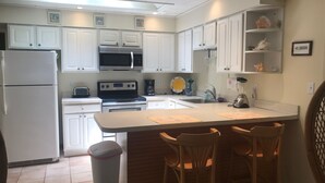 A kitchen with white cabinets, a microwave, a stove, a sink, and a trash can. There are two bar stools at the island. - Super Clean Home on a Quiet Cul-De-Sac in the Woods. (Lewes)