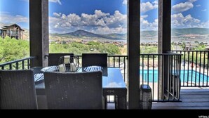 Un espace extérieur abrité comprenant une piscine, des chaises et une vue sur une montagne et une ville.