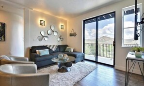 Ein modernes Wohnzimmer mit einem dunkelgrauen Sofa, einem Couchtisch und einem großen Fenster mit Blick auf eine gebirgige Landschaft.