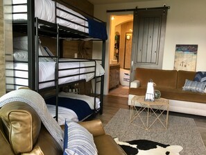 Ein Schlafraum mit Etagenbett, einem braunen Ledersofa, einem kleinen Beistelltisch und einem Kuhfellteppich.