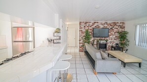 A modern kitchen with a stainless steel refrigerator, a marble countertop, and a built-in oven. There is a seating area with a grey sofa and a bench. - Balboa Back · Luxury Remodel Steps to Beach & Bay (Newport Beach)