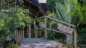 Un escalier en bois mène à un restaurant doté d’un toit de chaume et entouré d’une végétation luxuriante.