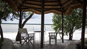 Un kiosque au bord de la plage, doté d’un toit de chaume, de deux chaises en bois et d’une table.